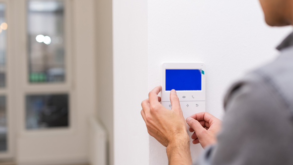 electronic alarm system on office wall being set by person in shirt